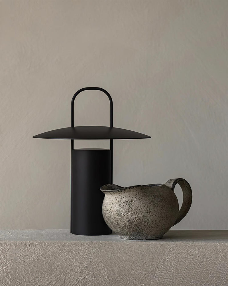 Cordless lantern lamp PORTO No.01 in black lit next to a stone pitcher on a plaster surface