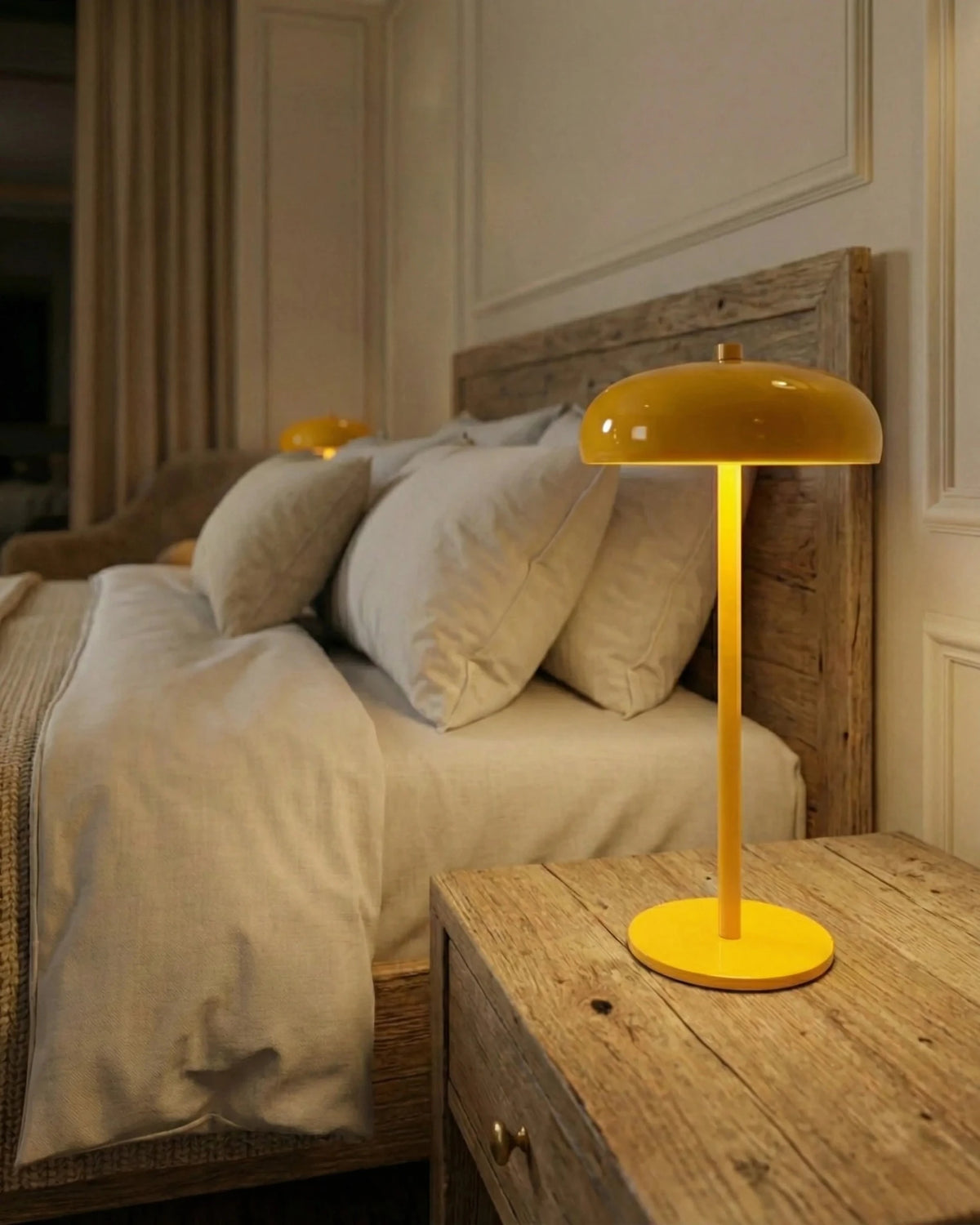 Cordless mushroom lamp DOMA No.01 in yellow lit on a rustic wooden nightstand beside a bed with white linens
