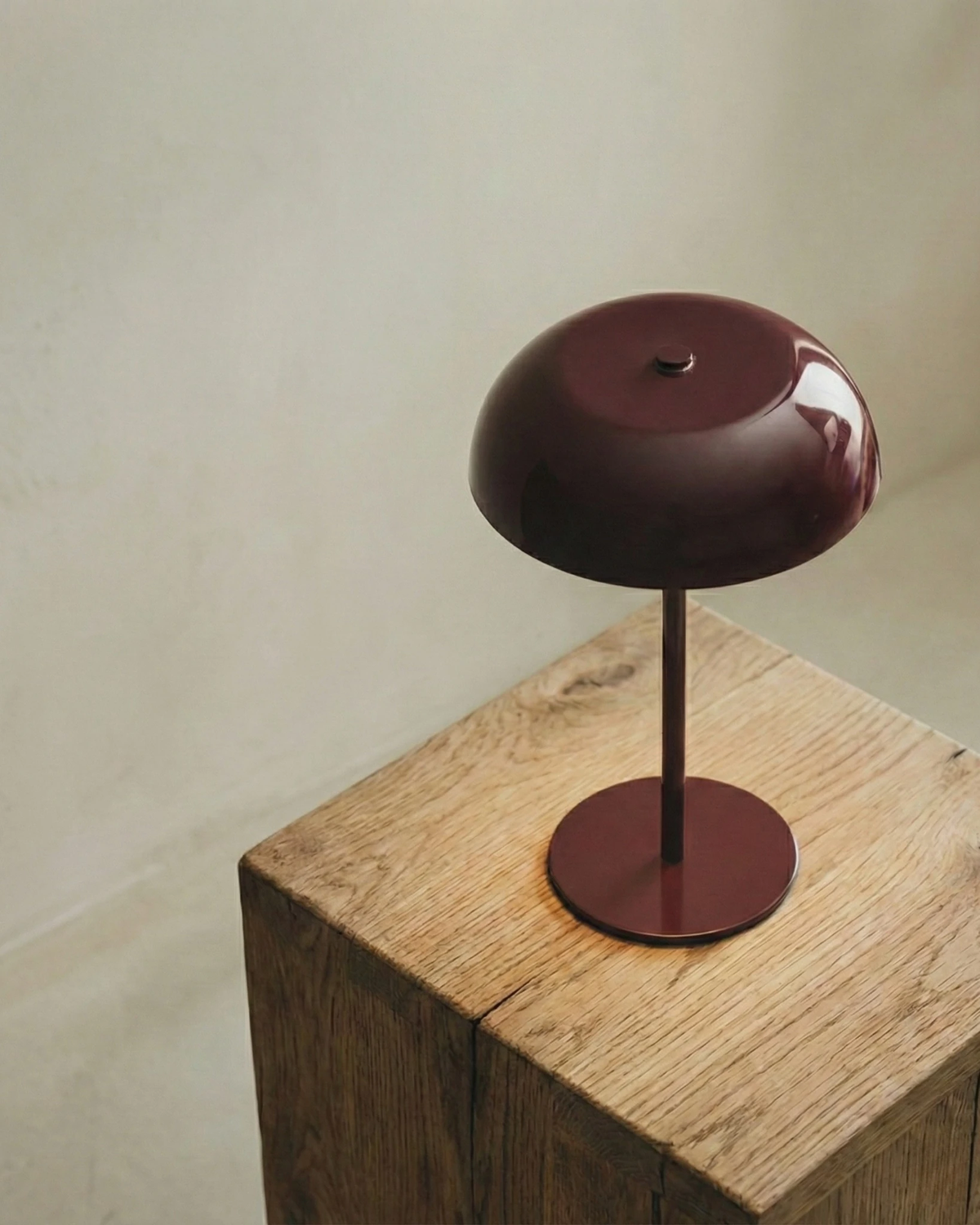 Cordless mushroom lamp LUMA No.02 in Bordeaux Red standing on a solid oak block plinth against a plaster wall