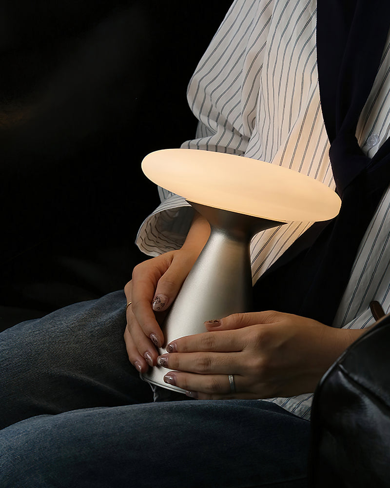 Cordless mushroom lamp DOMA No.03 glowing in the hands of a seated person wearing a striped shirt