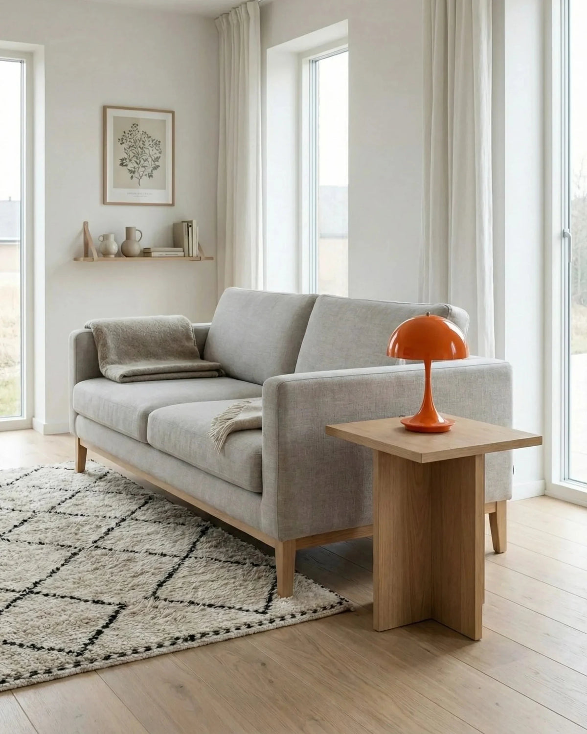 Cordless mushroom lamp FONTE No.01 in sun orange on a wooden side table beside a grey sofa by tall windows