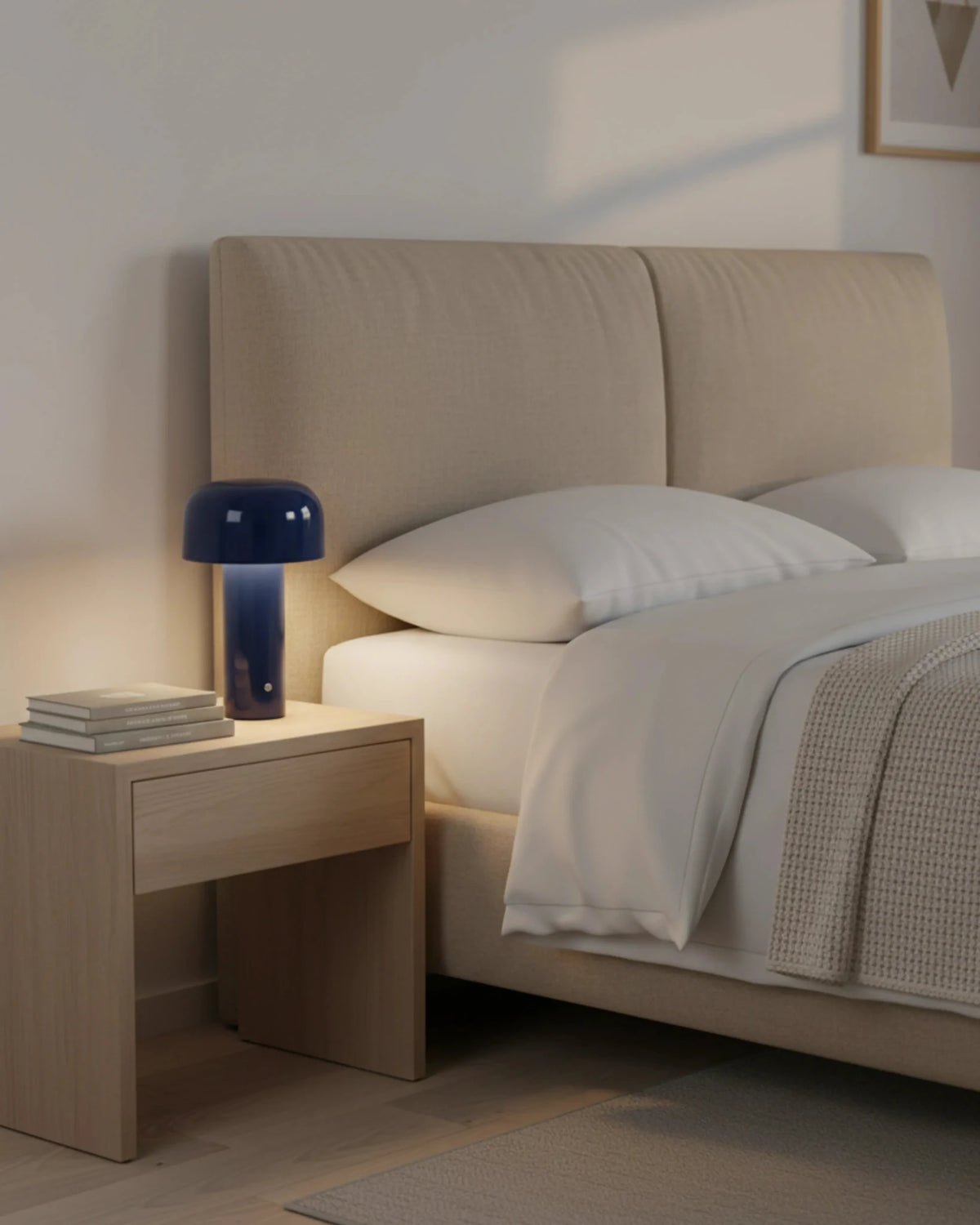 Cordless table lamp DOLCE No.01 in royal blue switched on atop a wooden nightstand beside a white bed