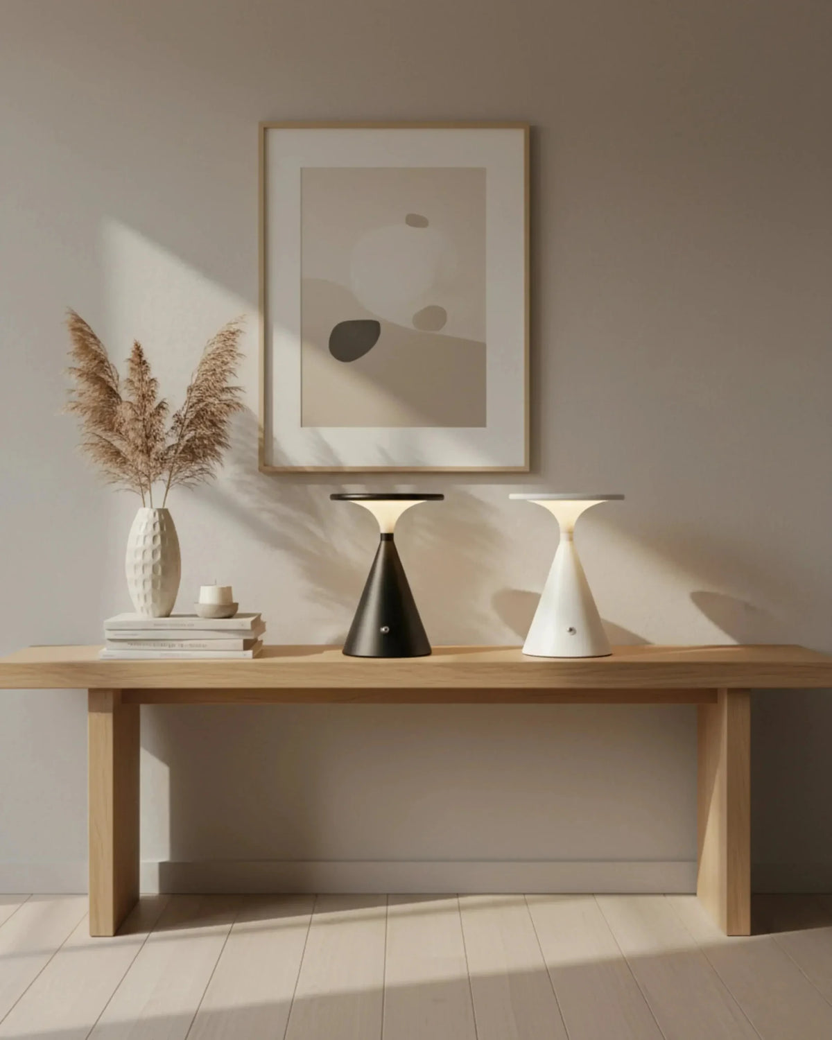 Two cordless table lamps SOSTA No.01 in black and warm white lit on a light oak console with framed art