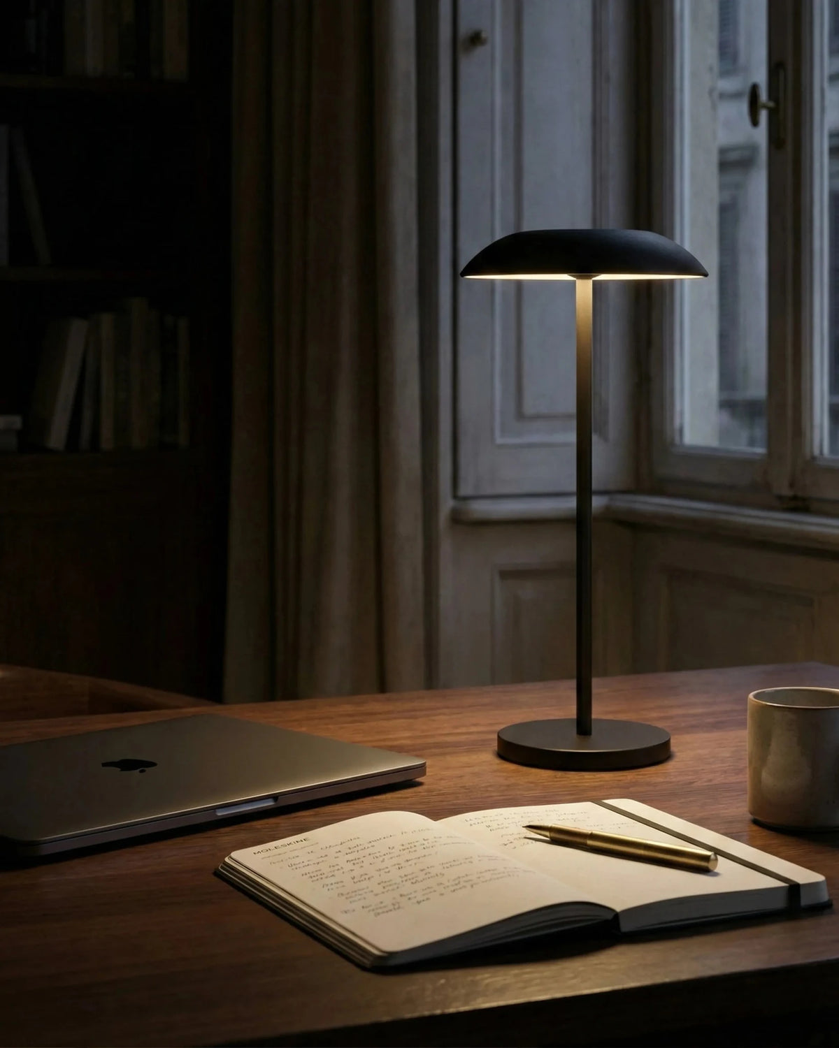 Cordless table lamp PESCARA No.01 in black switched on at a desk with a laptop and open notebook by a window
