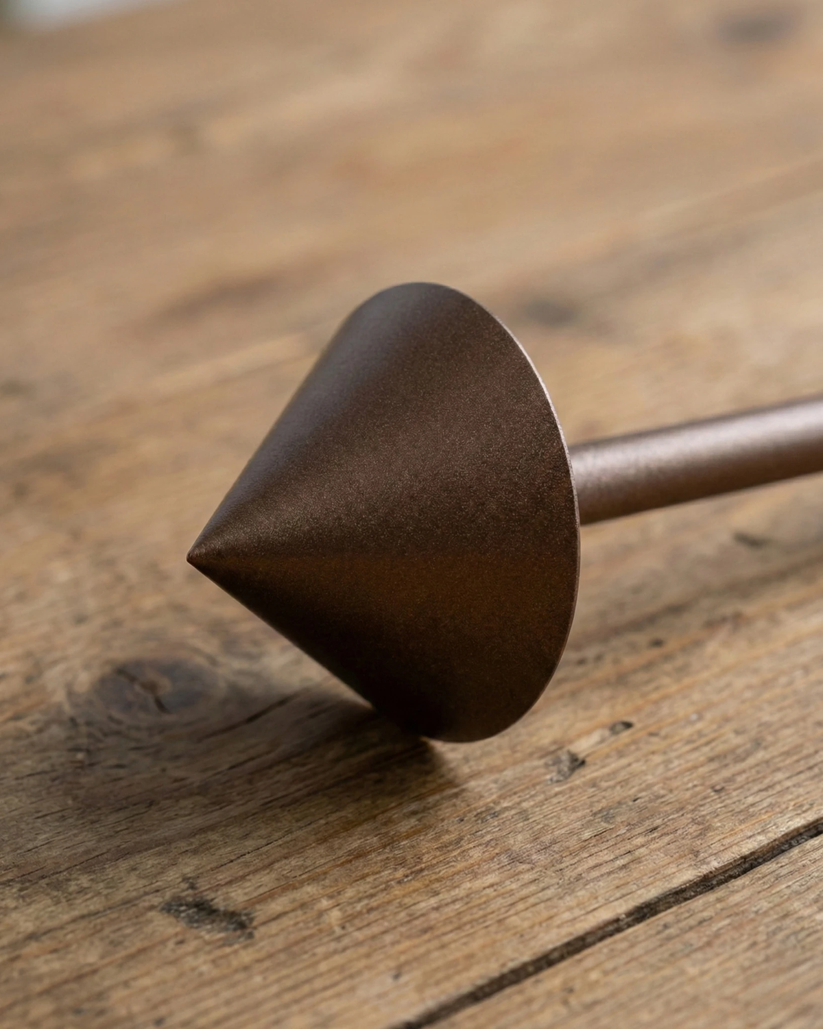 Close-up of the brushed brown cone head of the FERRARA No.01 cordless table lamp lying on a wooden surface