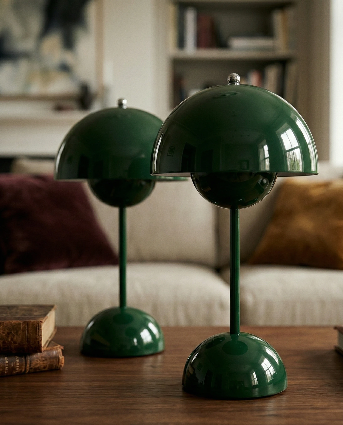 Two cordless table lamps DOMA No.02 in dark green side by side on a wooden table in front of a sofa, unlit