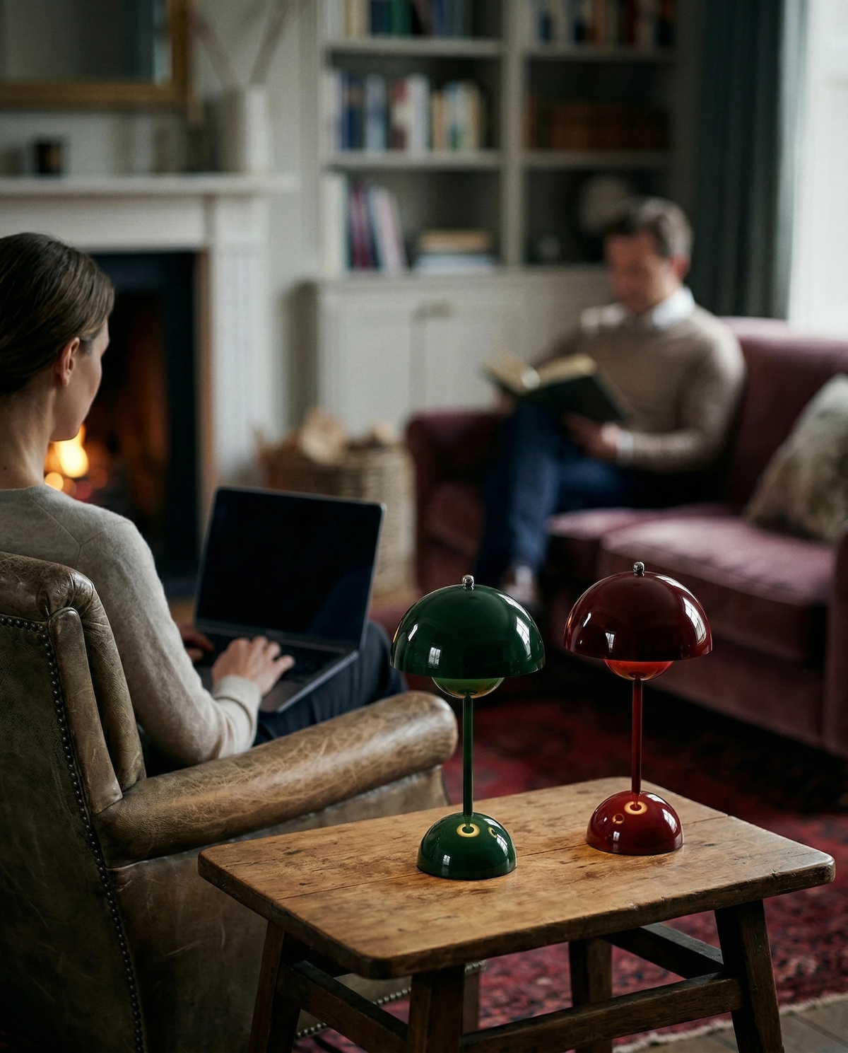 Two cordless table lamps DOMA No.02, green and wine red, lit on a wooden stool table in a living room by the fire