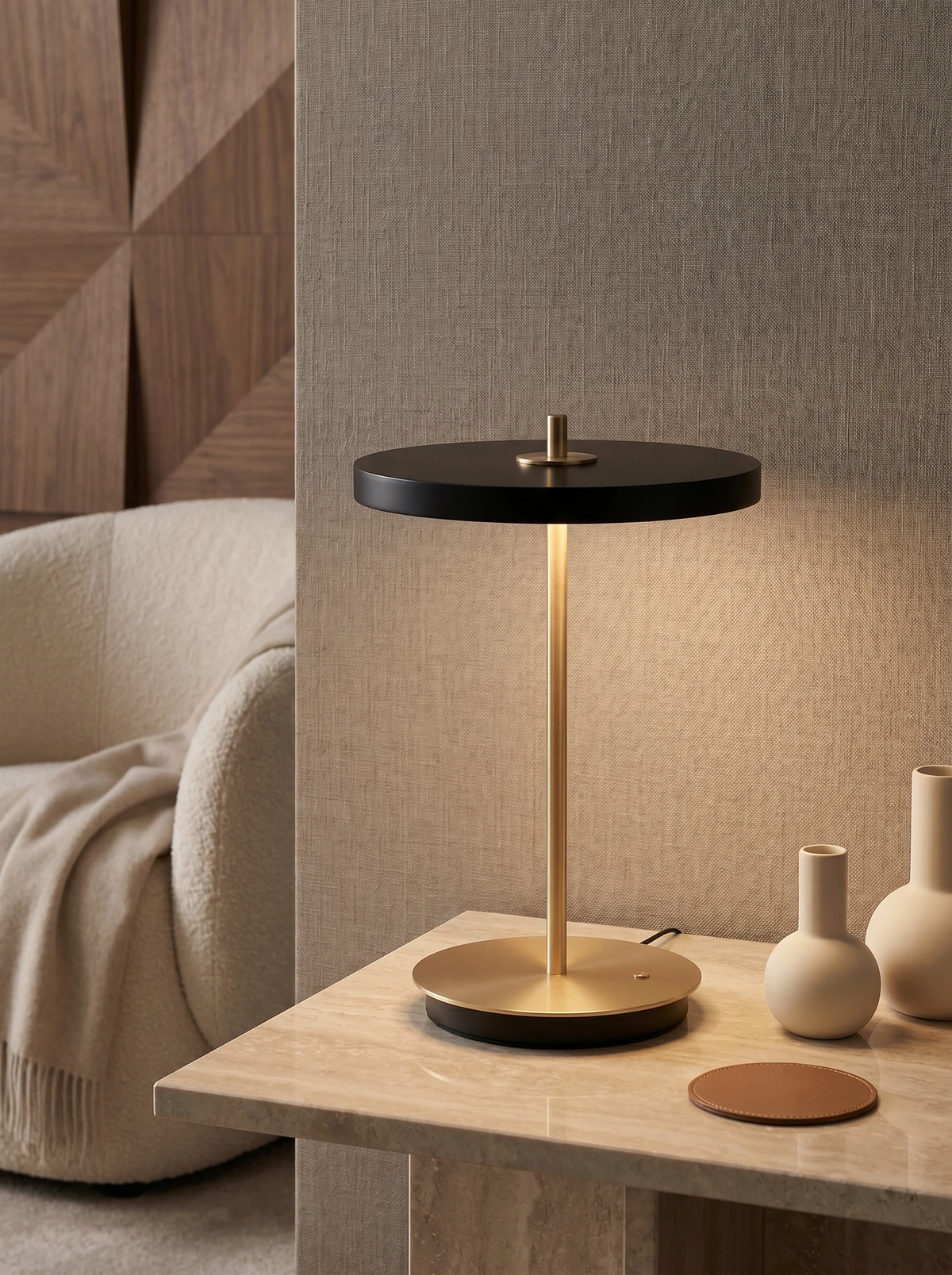 Cordless table lamp SALA No.01 in matte black, lit on a travertine side table beside a boucle sofa with vases
