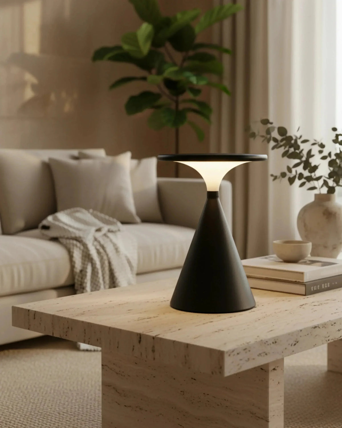 Cordless table lamp SOSTA No.01 in black lit on a travertine coffee table beside a cream sofa