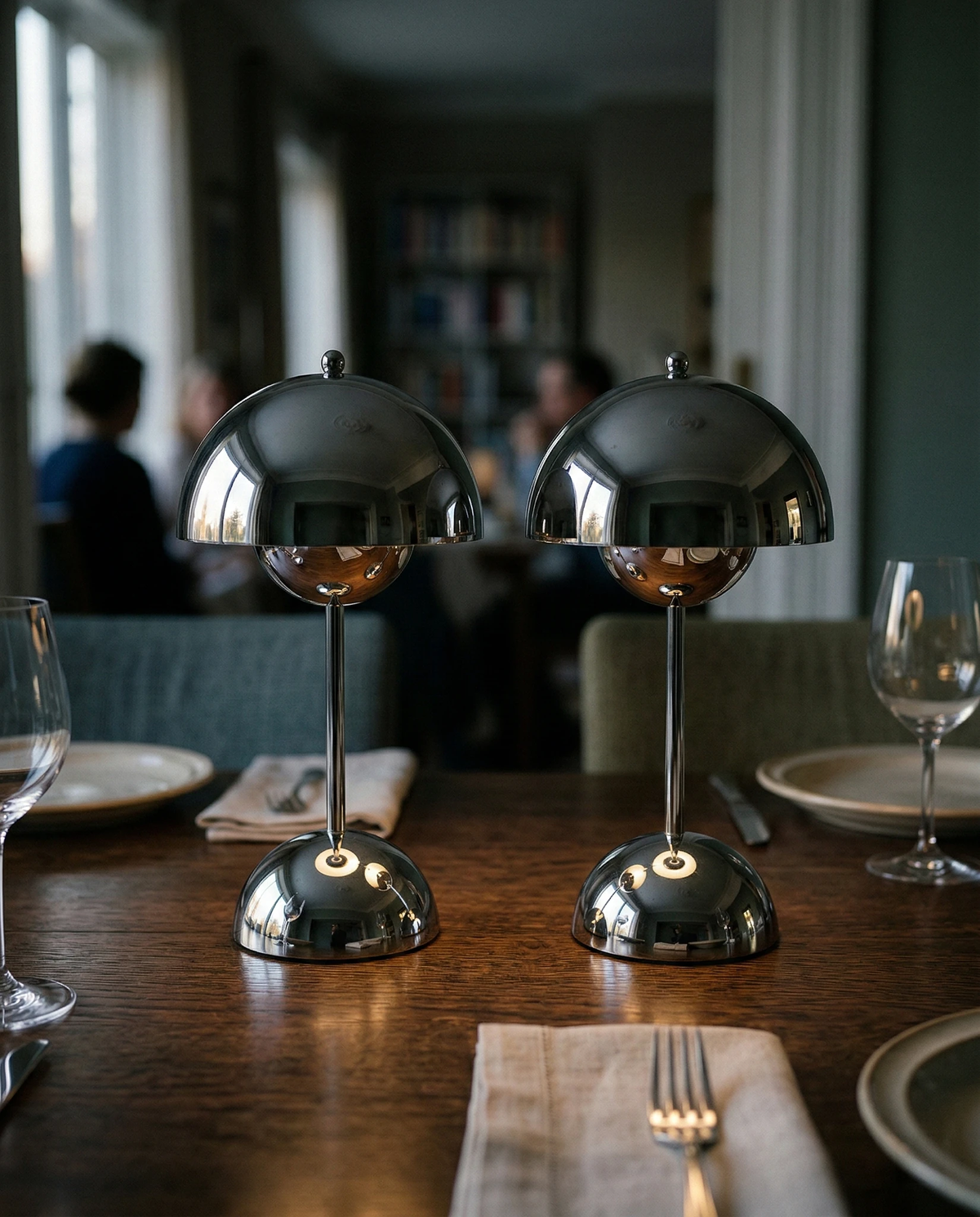 Two cordless table lamps DOMA No.02 in polished silver lit on a set restaurant table with wine glasses