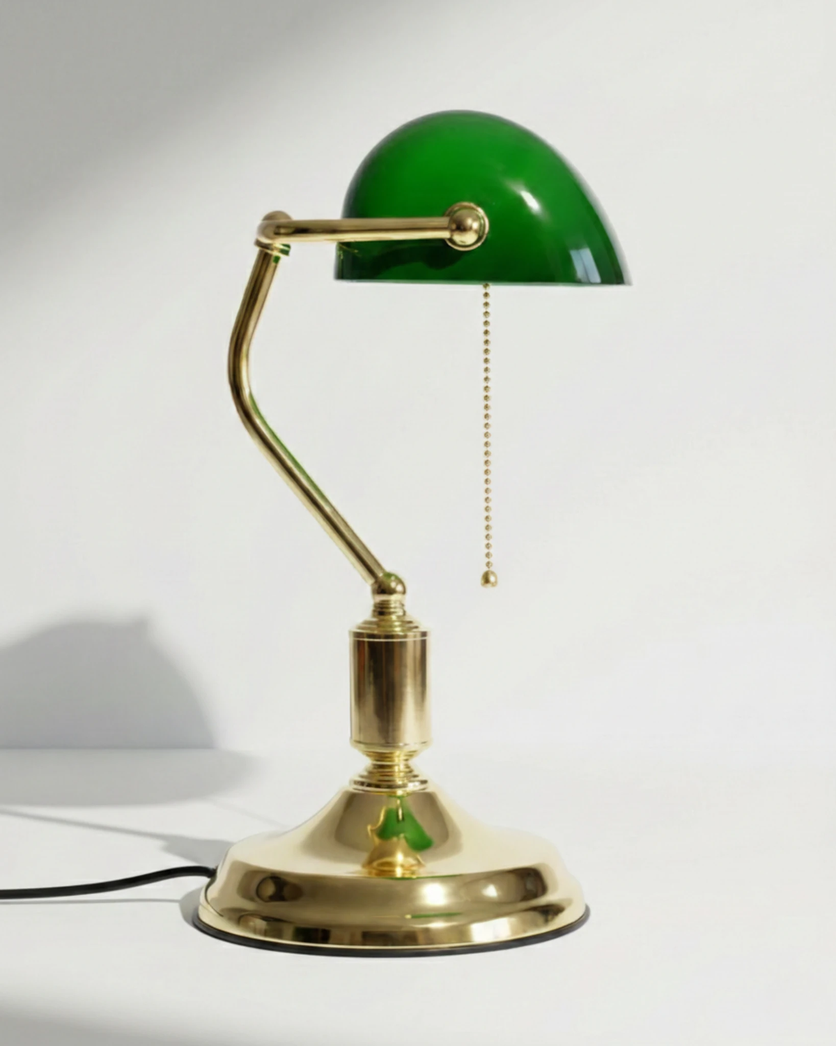 Glass desk lamp BANCO No.01 in green with a curved brass arm and domed shade on a polished brass base, unlit