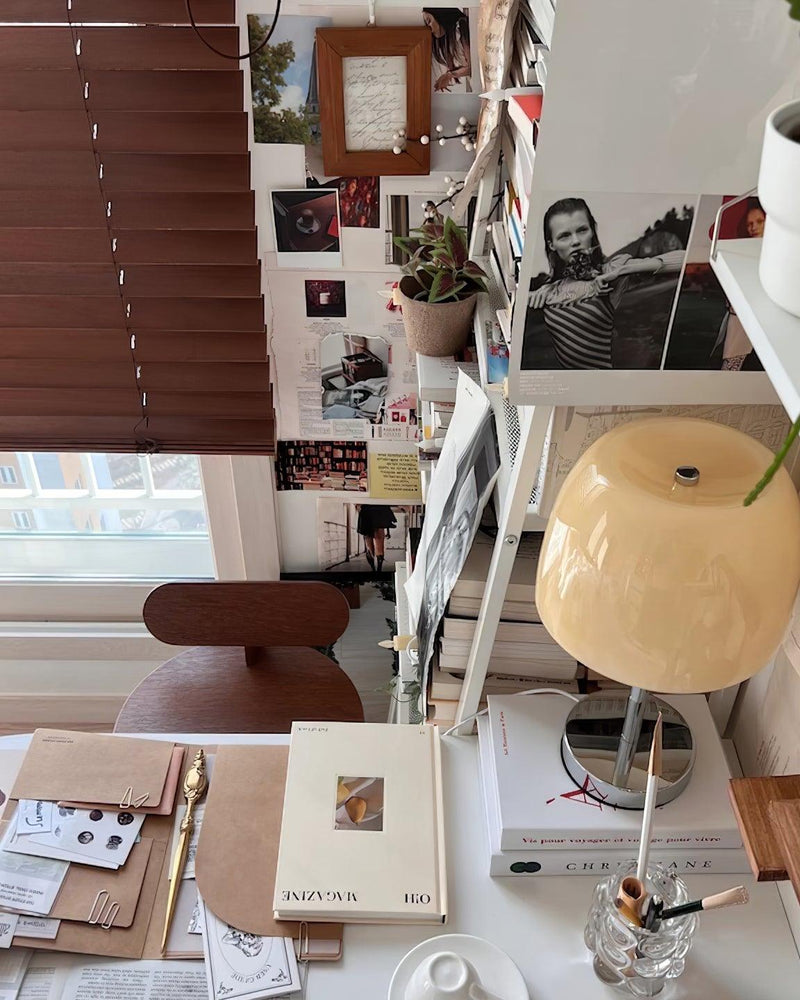 Glass table lamp VENEZIA No.01 with cream shade on a desk with books, window blinds and a photo wall behind