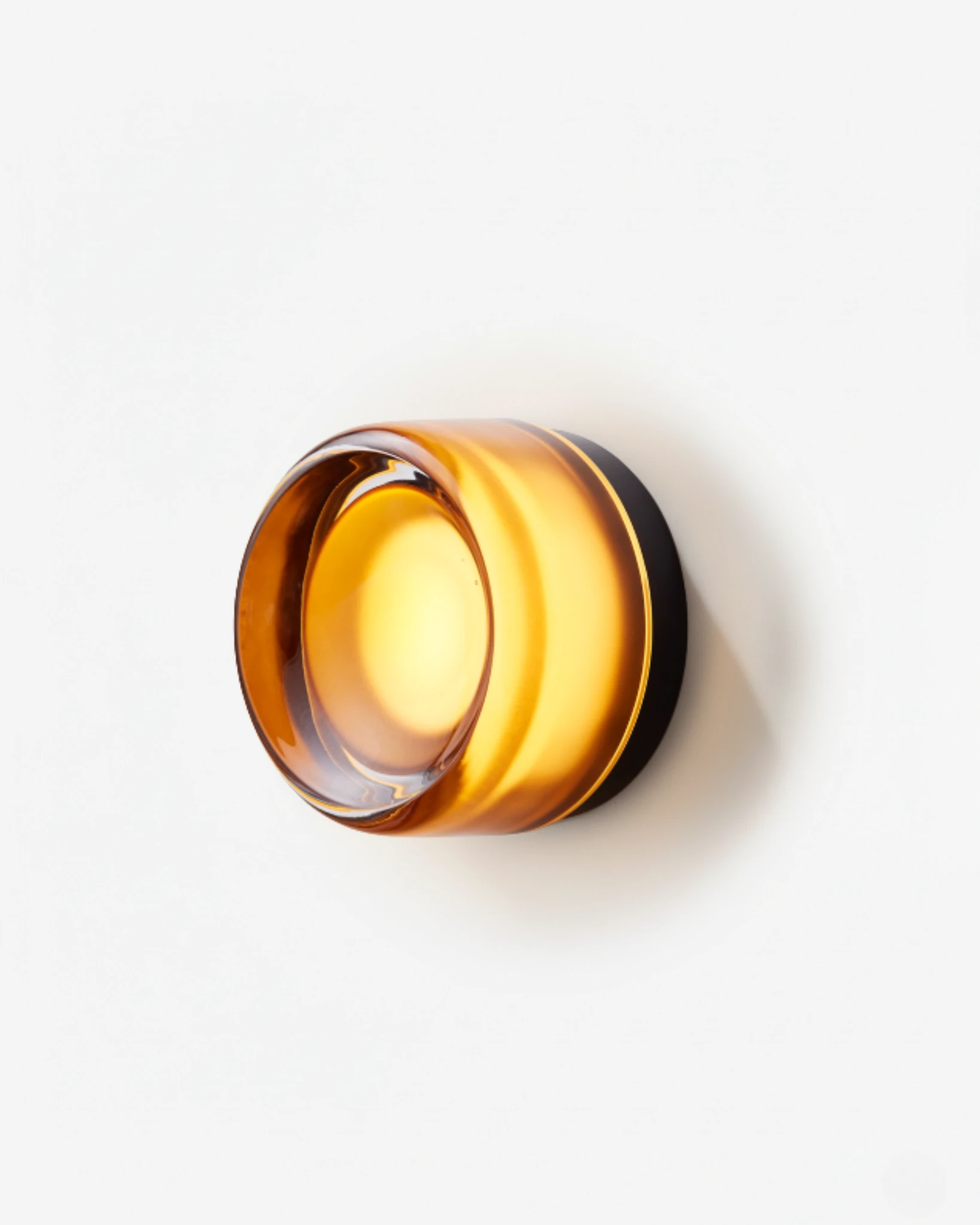 Glass wall sconce HALO No.08 in Amber Noir, amber glass ring on a black base, switched on