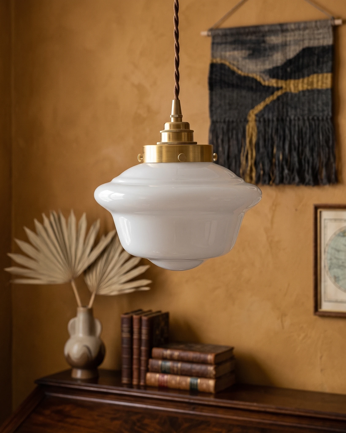 Globe pendant light SCOLA No.01 with opaline schoolhouse shade and brass fitter above a sideboard with books on an ochre wall