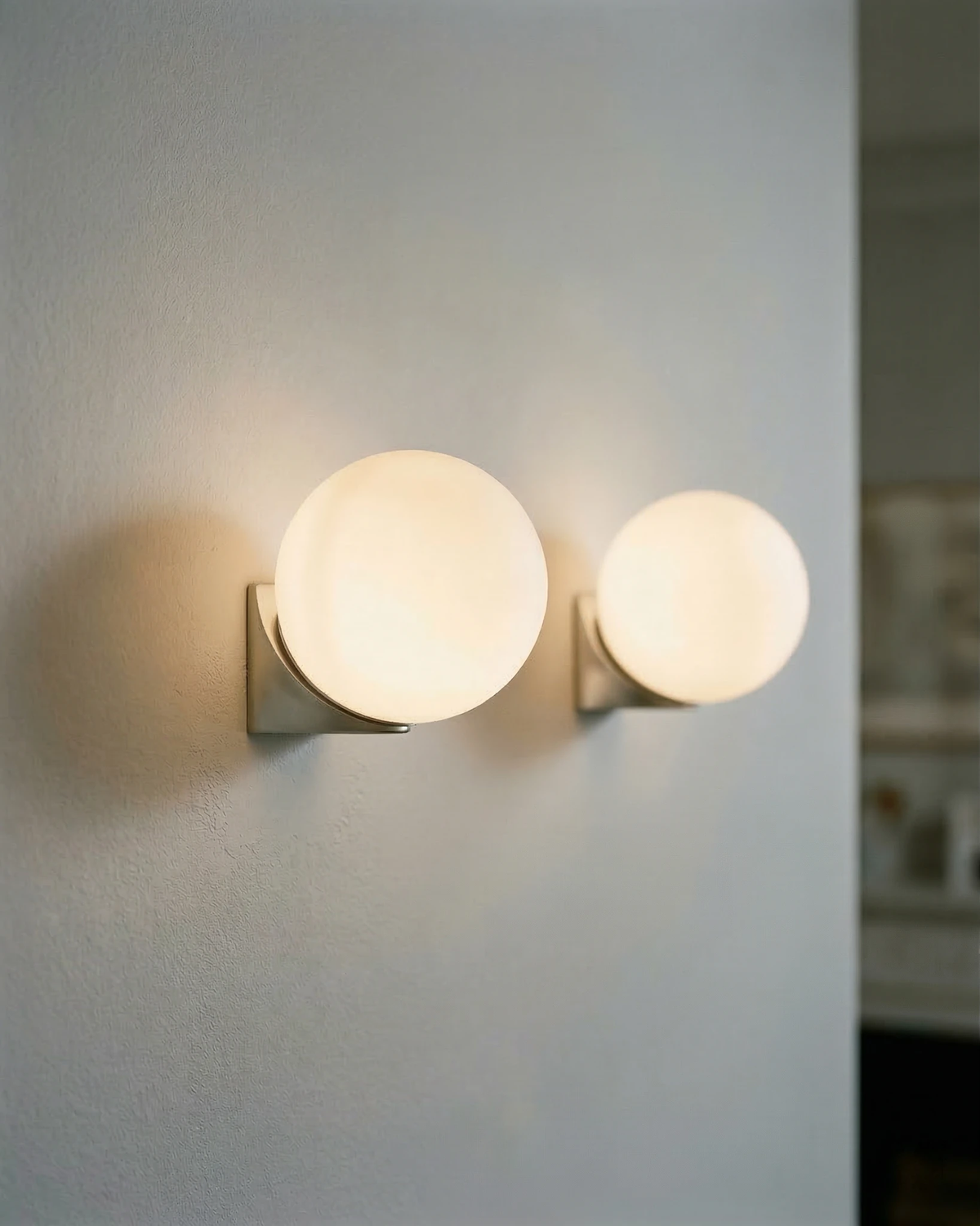 Two globe wall sconces AURA No.03 single lit side by side, one on a brass bracket and one on silver