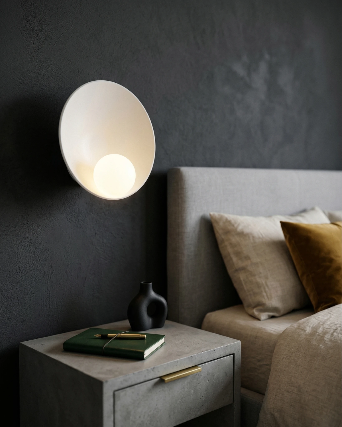 Globe wall sconce OASI No.01 in pure white, lit on a dark wall above a nightstand next to a bed