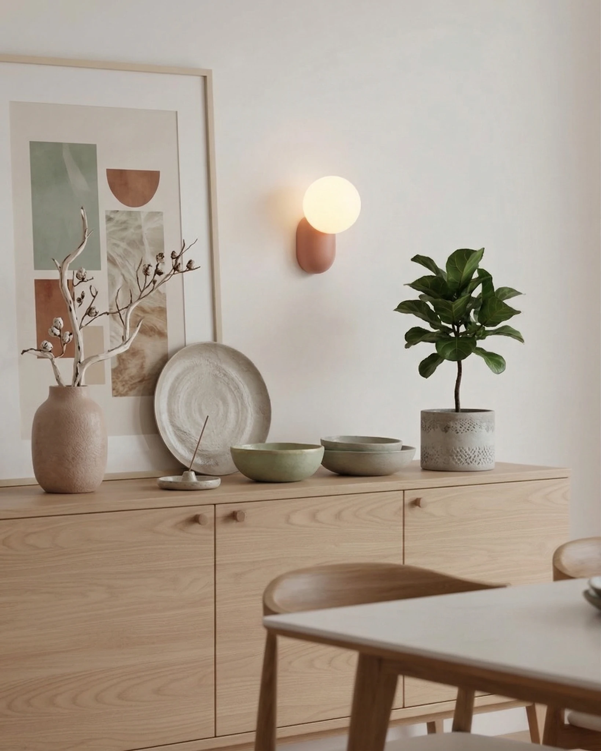 Globe wall sconce AURA No.04 in powder pink lit above a light oak sideboard with ceramics and a plant