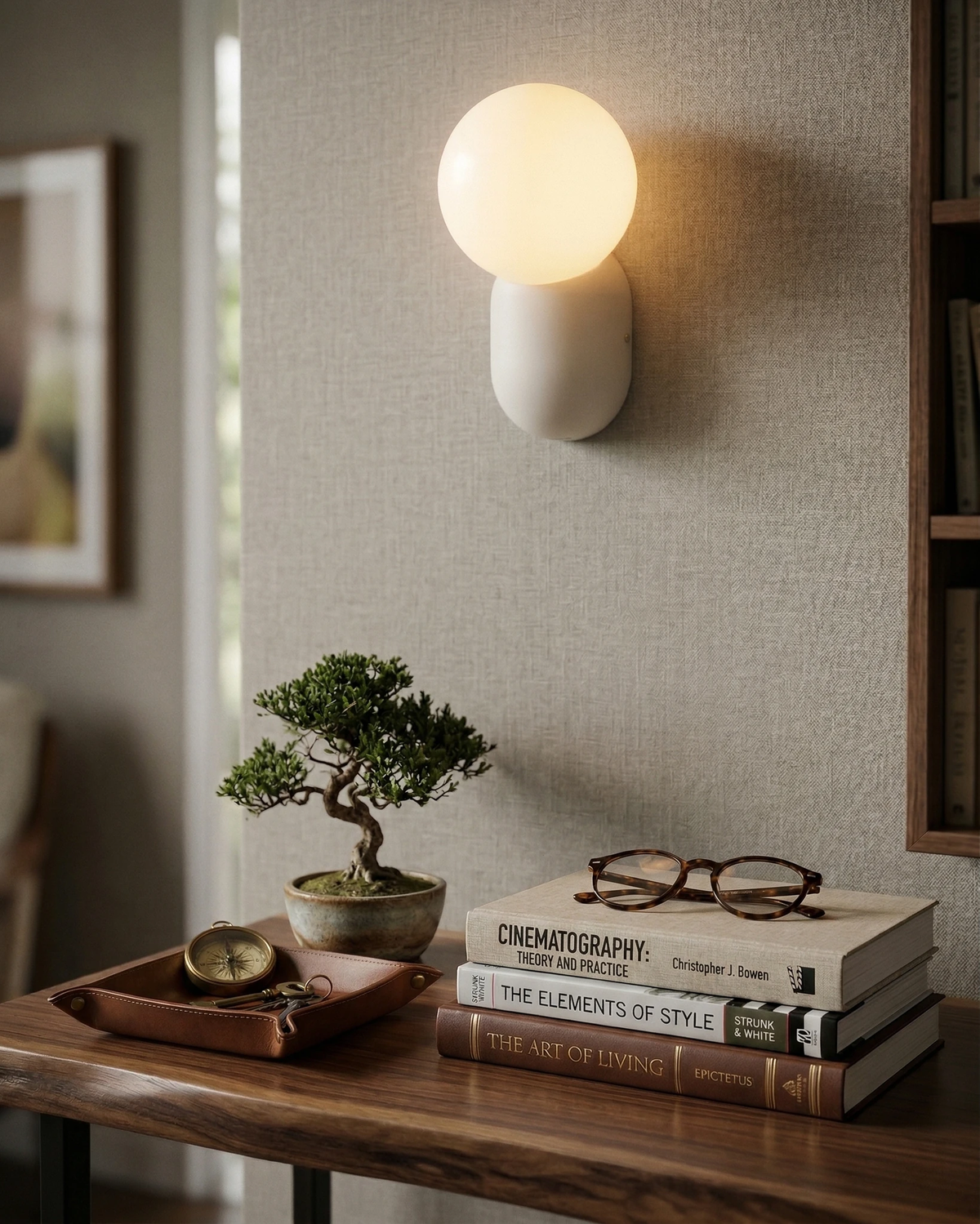 Globe wall sconce AURA No.04 in cream white lit above a wooden desk with books, glasses and a bonsai