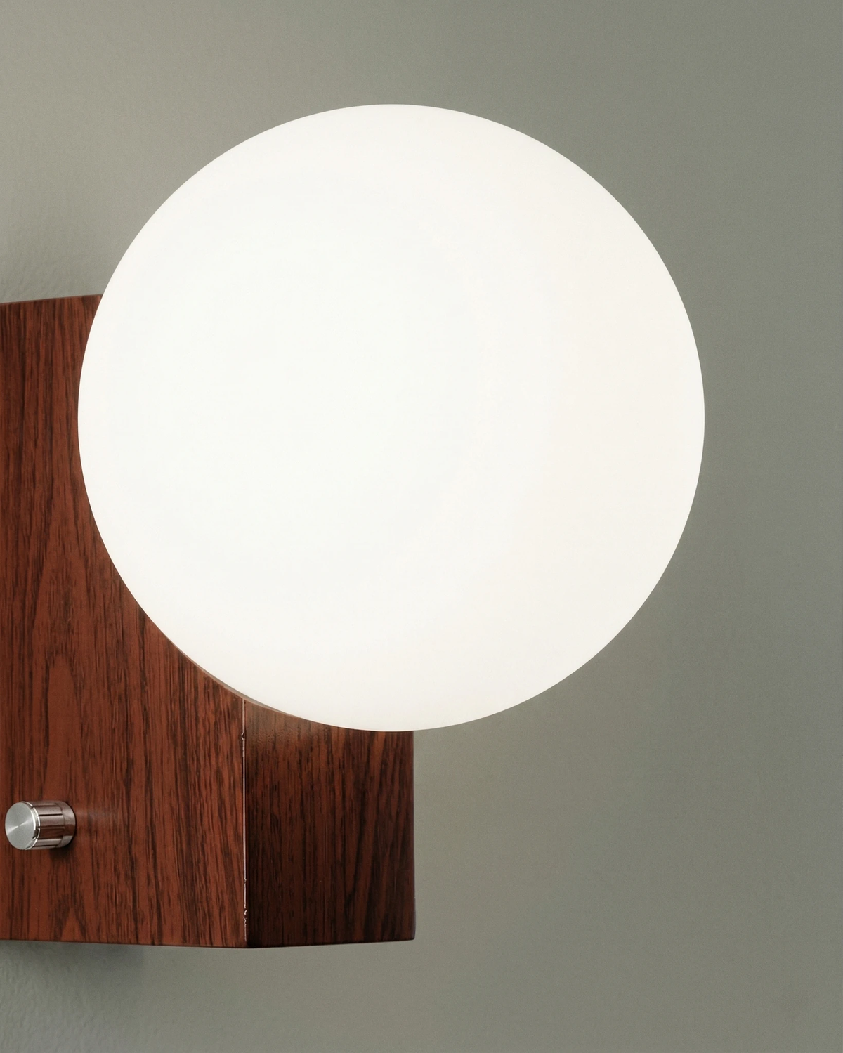 Close-up of the walnut block and white opal globe of the globe wall sconce ELBA No.01 on a gray wall