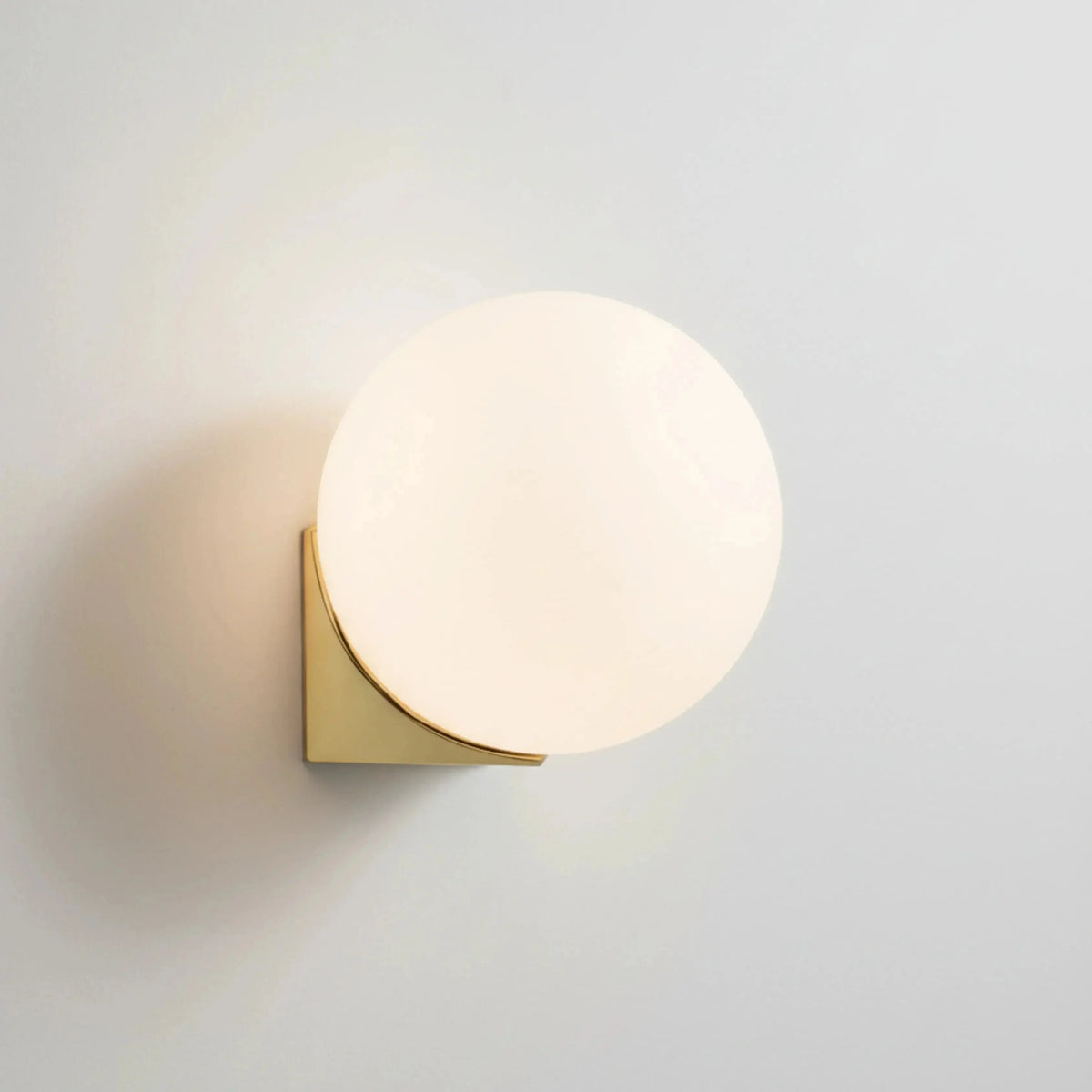 Globe wall sconce AURA No.03 single, opal glass globe switched on above a brushed brass wall plate