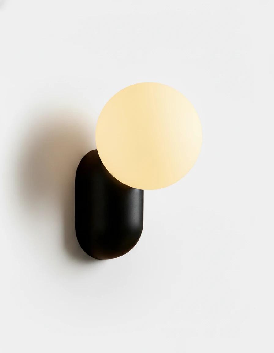 Globe wall sconce AURA No.04 in Volcano Black, opal glass globe glowing on a black resin capsule