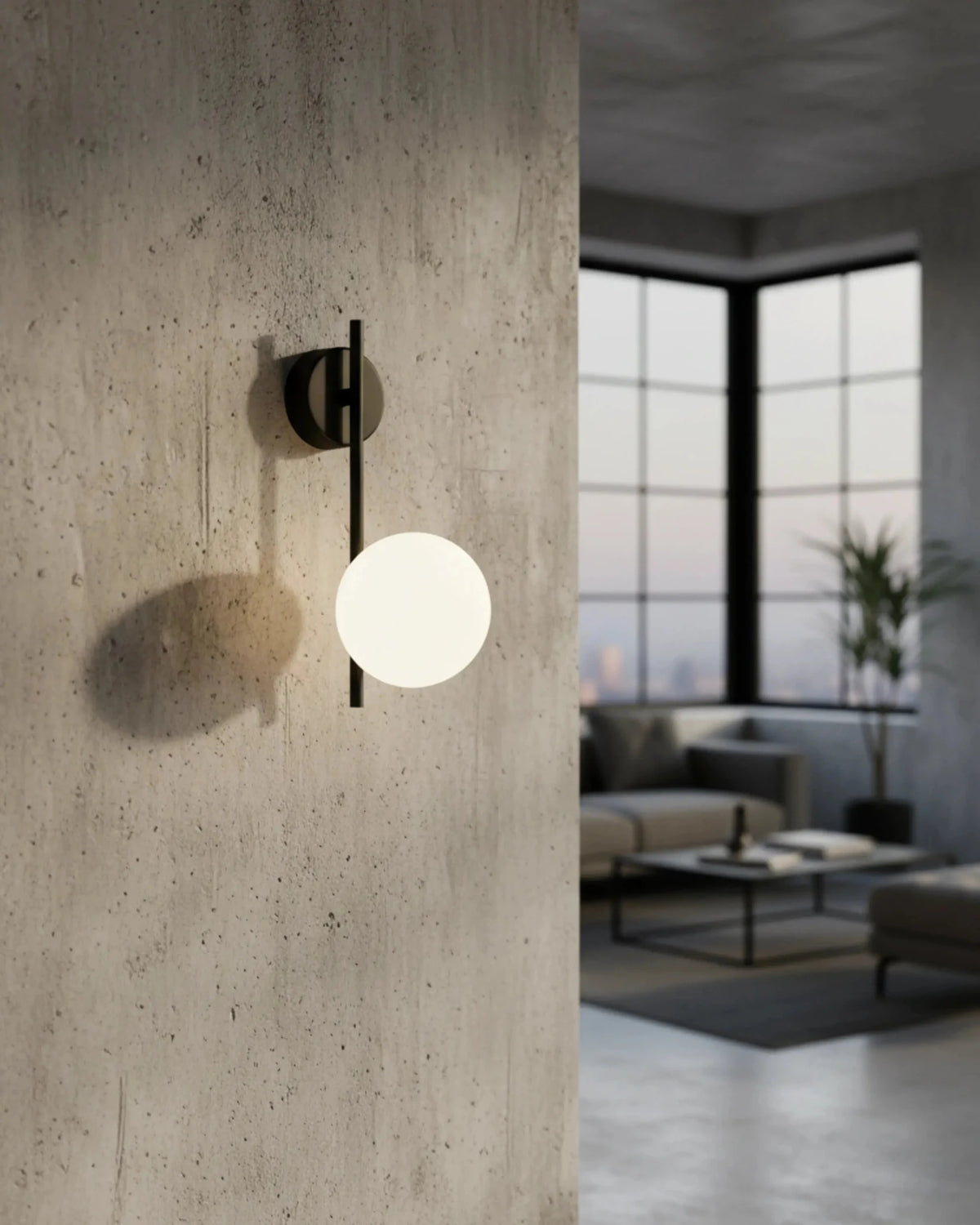 Globe wall sconce ASTRO No.01 in matte black on a concrete pillar with a sofa and tall windows beyond