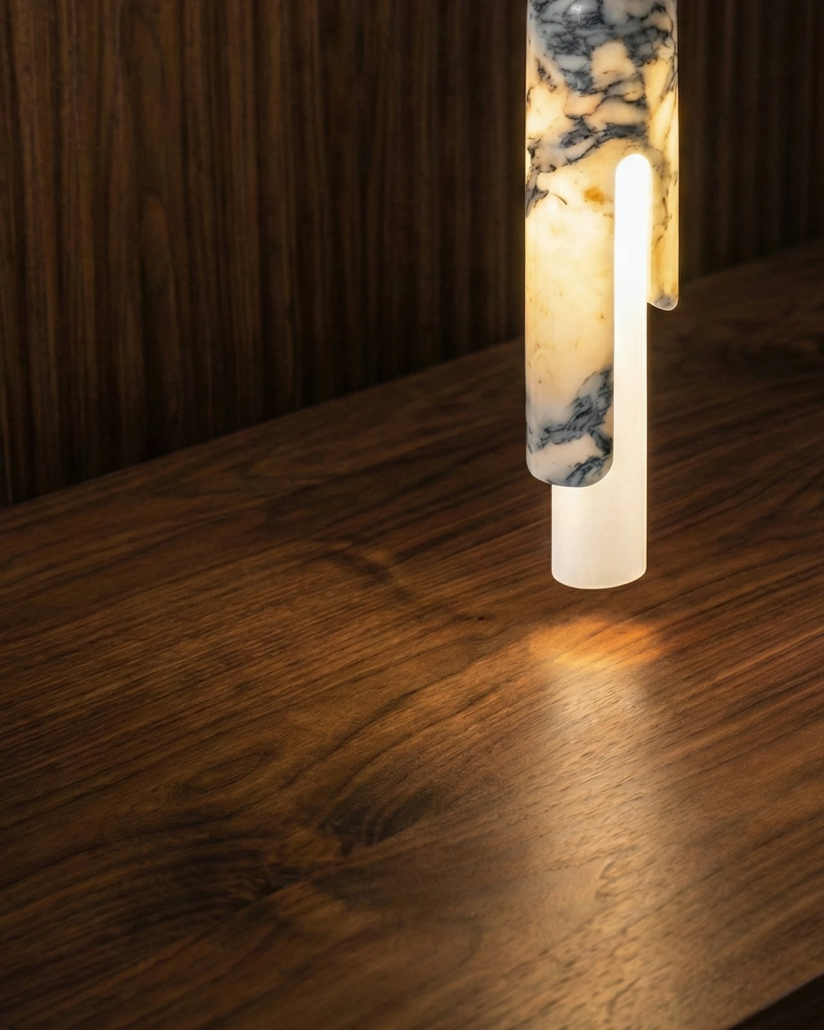 Close-up of the lit PALERMO No.01 marble pendant light hanging low over a dark walnut surface