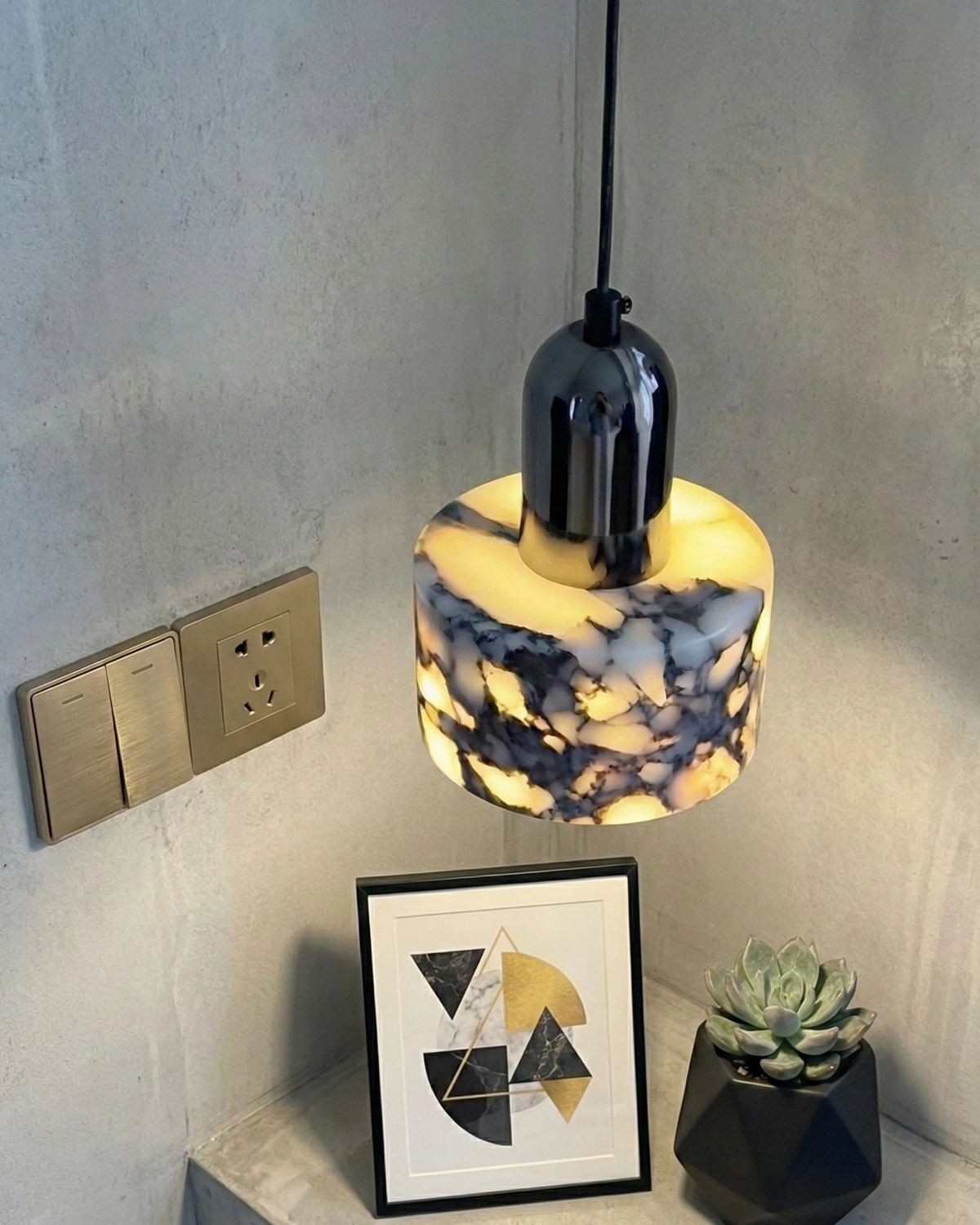 Marble pendant light MARMI No.02 switched on in a concrete corner above a framed print and a succulent