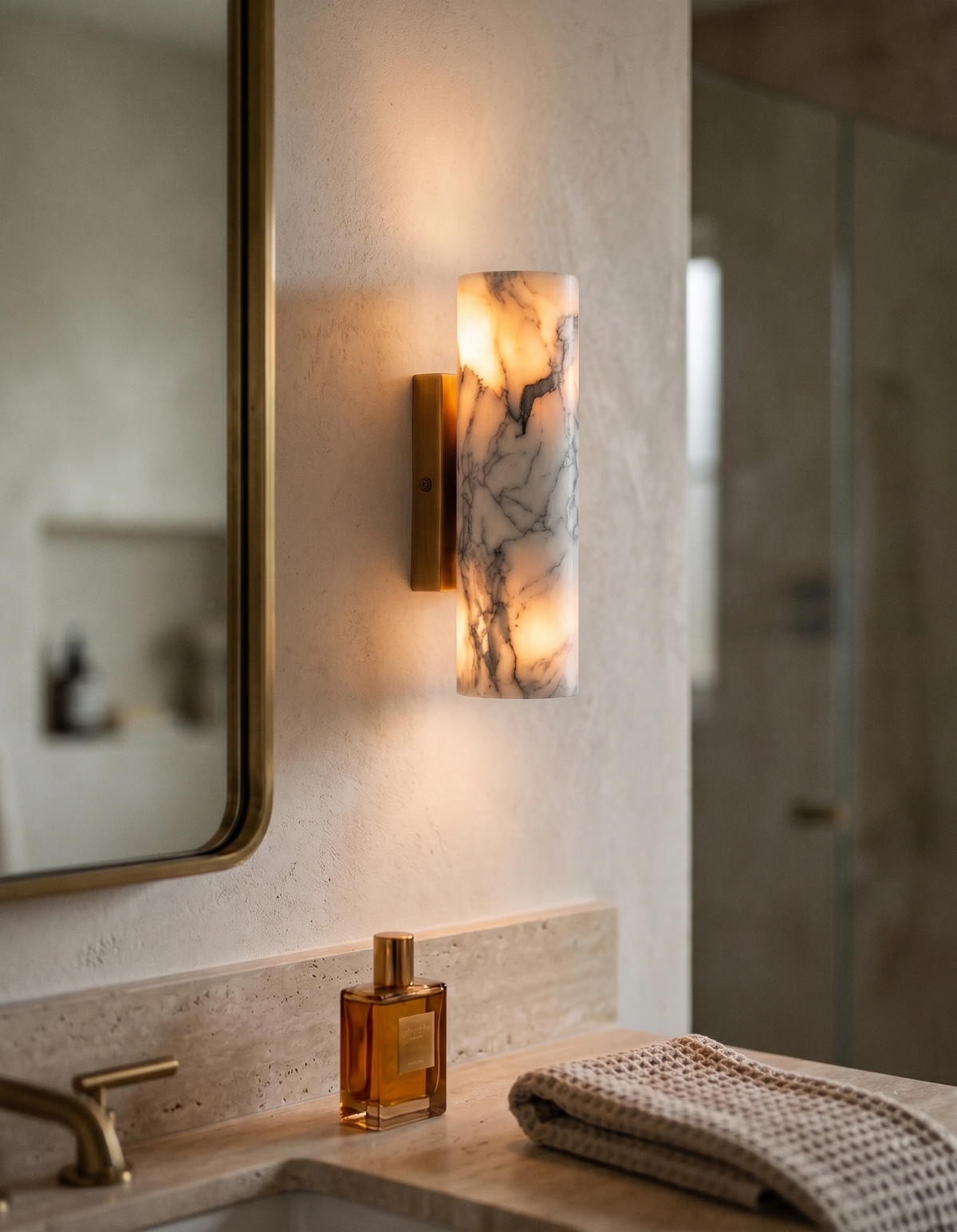 Marble wall sconce PORTORO No.01 lit beside a mirror above a stone bathroom counter with bottles