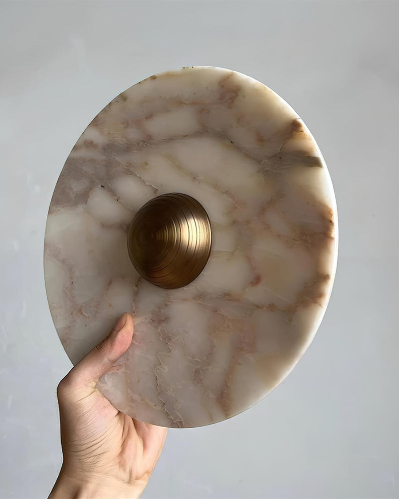 Close-up of the brass-centered marble disc of the LATTE No.01 marble wall sconce held up by hand to show its size