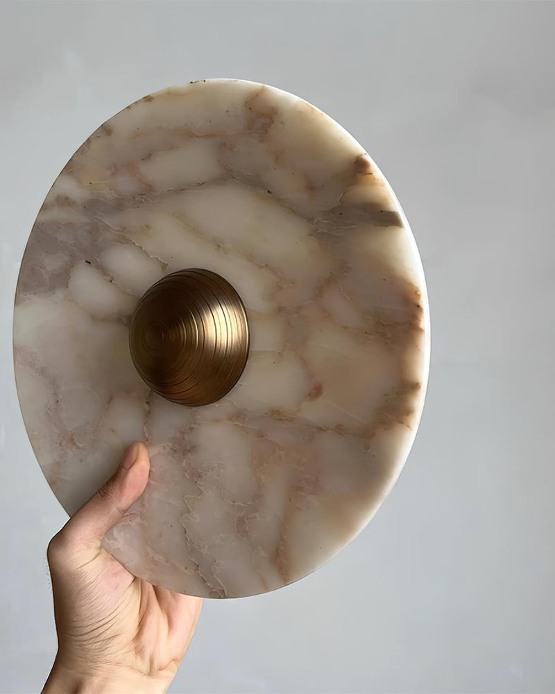 Close-up of a hand tilting the LATTE No.01 marble wall sconce to show the veined marble surface and brass center