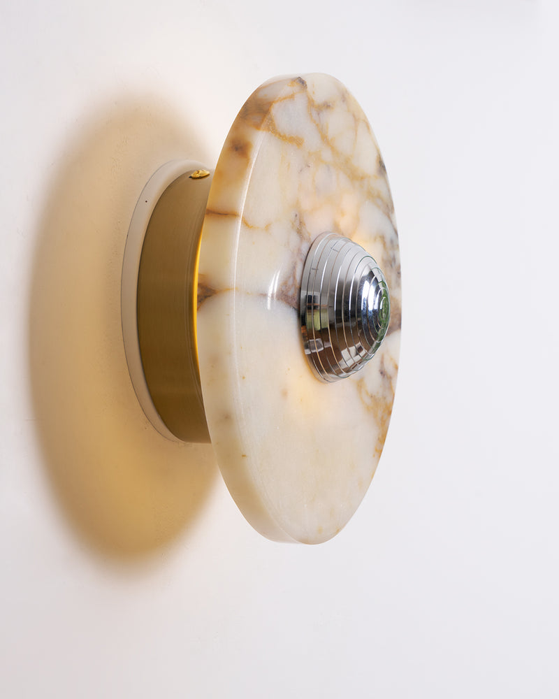 Close-up side view of the LATTE No.01 marble wall sconce lit, chrome dome on a gold-veined disc with a brass backplate