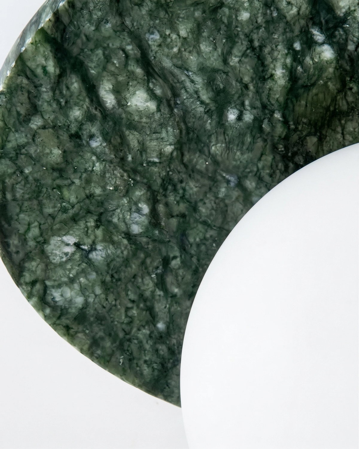 Close-up of the green marble backplate meeting the opal globe on the VENA No.01 marble wall sconce