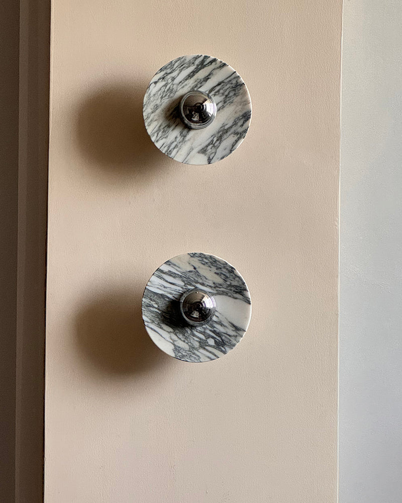 Two marble wall sconces LATTE No.01 in chrome mounted one above the other on a beige wall, unlit