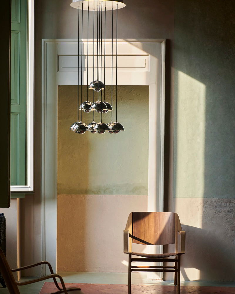 Modern chandelier FLORA No.01 with chrome mirror globes hanging in a green plastered room beside a wooden armchair