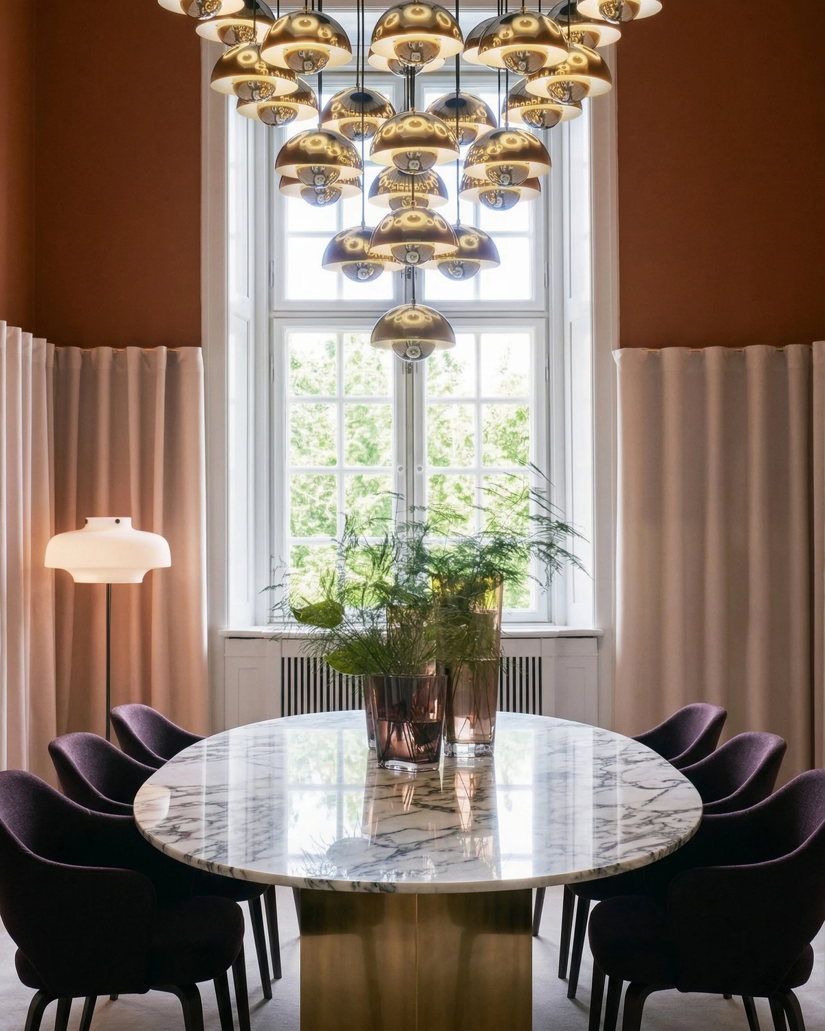 Modern chandelier FLORA No.01 with polished metallic globes above a long oval marble dining table and dark chairs