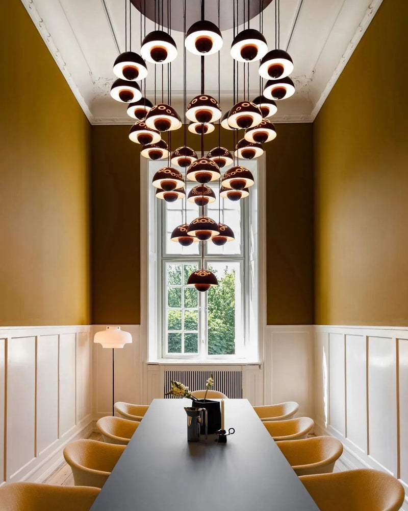 Modern chandelier FLORA No.01 cascade of deep red petal globes, lit, over a long dining table with mustard chairs