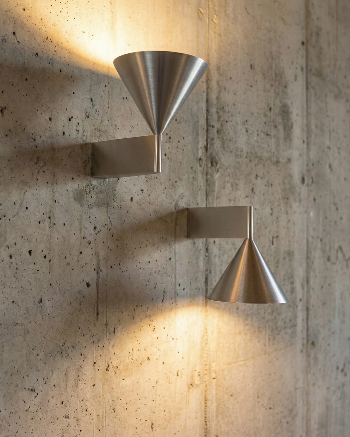 Two modern wall sconces ETNA No.01 in aluminum on a concrete wall, one cone up and one cone down, lit