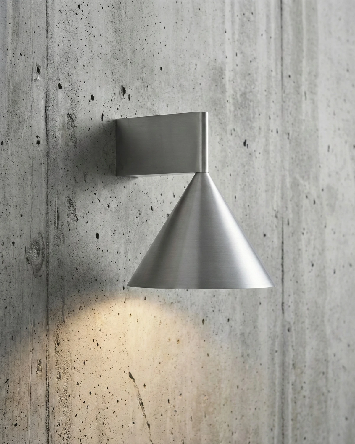 Modern wall sconce ETNA No.01 in aluminum mounted cone-down on a raw concrete wall, casting light below