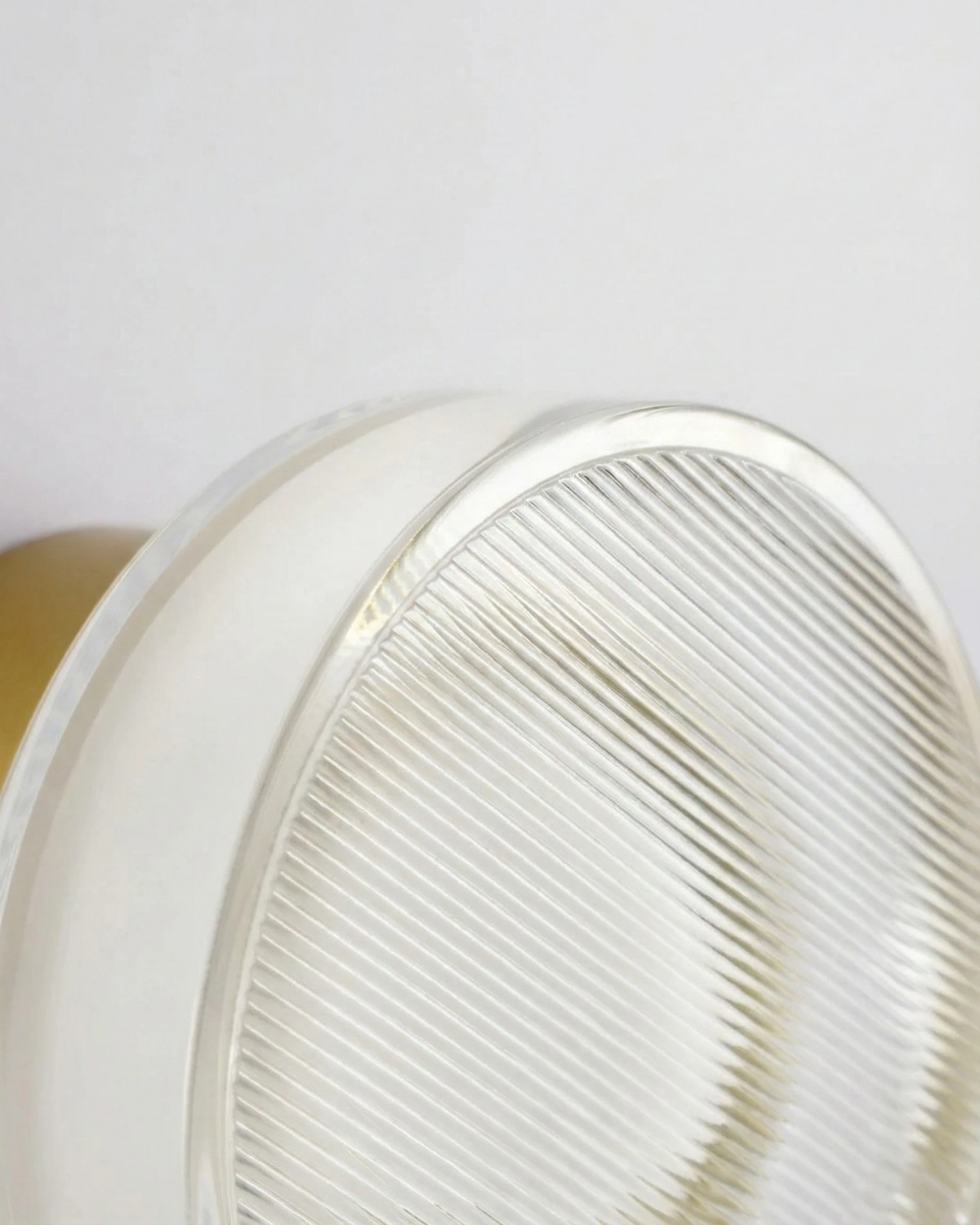 Close-up of the ribbed fluted acrylic disc edge of the OBLI No.01 modern wall sconce with a brass base