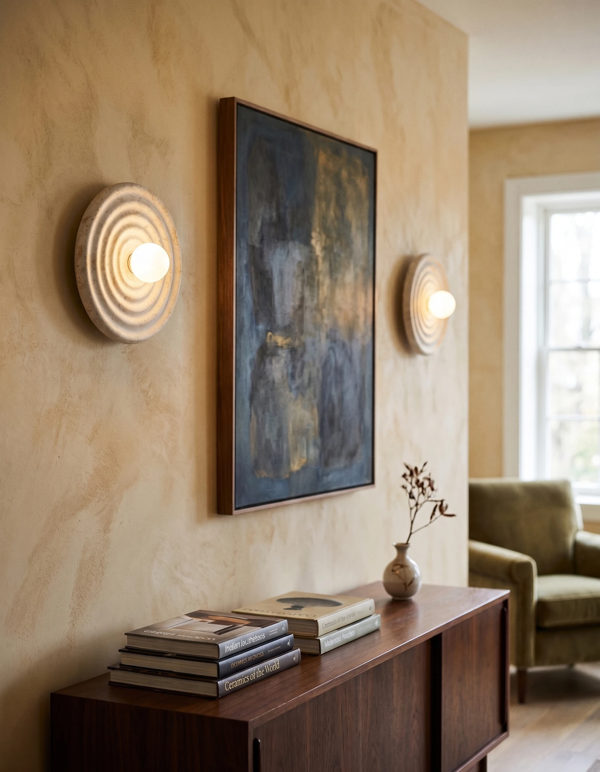 Modern wall sconce ANIMA No.01 switched on beside a painting above a wood sideboard in a living room