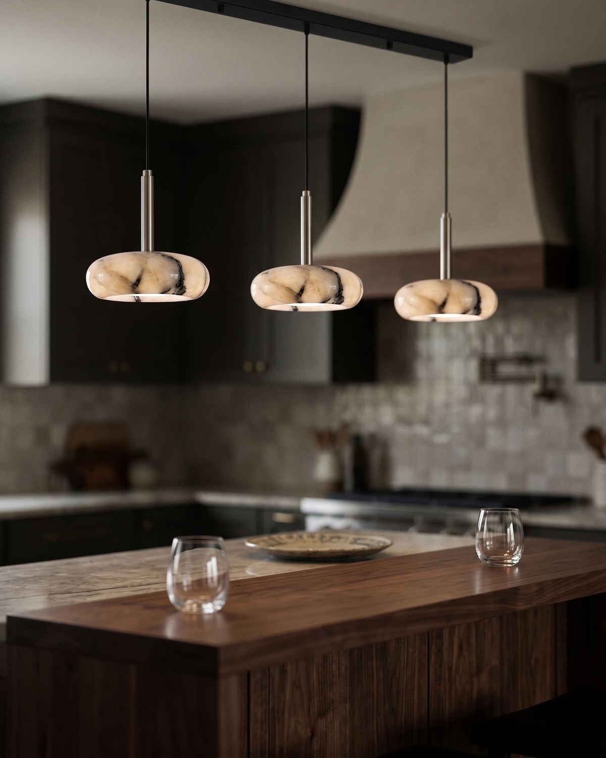 Onyx pendant light TIBER No.01 three-head bar lit over a walnut island in a dark kitchen with a plaster hood