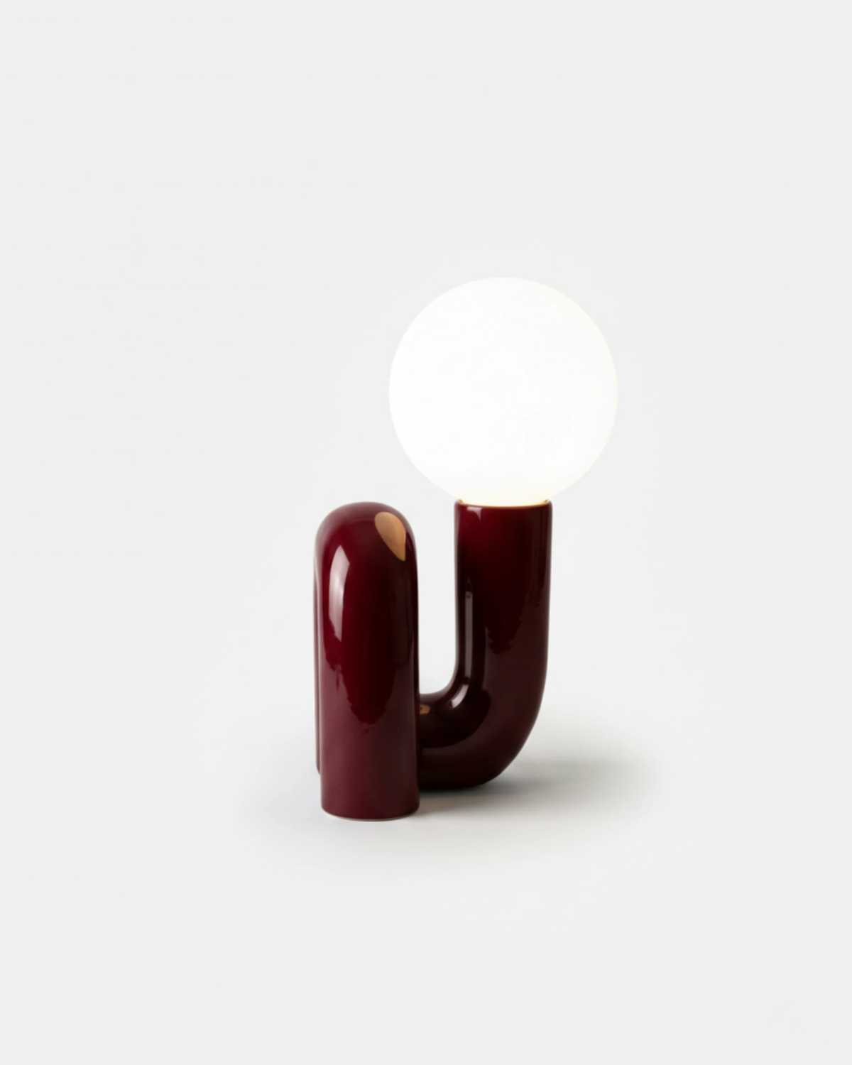 Opal globe table lamp VICO No.01 in Bordeaux Red, glossy curved resin base with the globe switched on