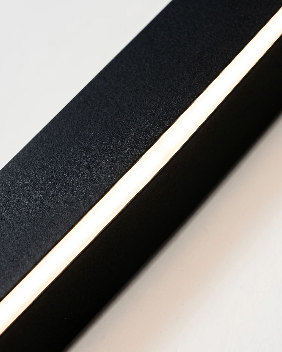 Close-up of the matte black aluminum profile of the outdoor wall sconce FRECCIA No.01 with its edge-lit LED strip glowing
