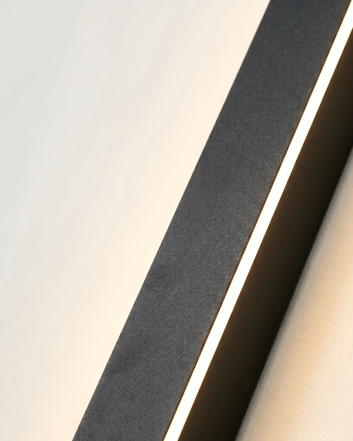 Close-up of the outdoor wall sconce FRECCIA No.01, black bar lit from the side showing the slim LED light edge