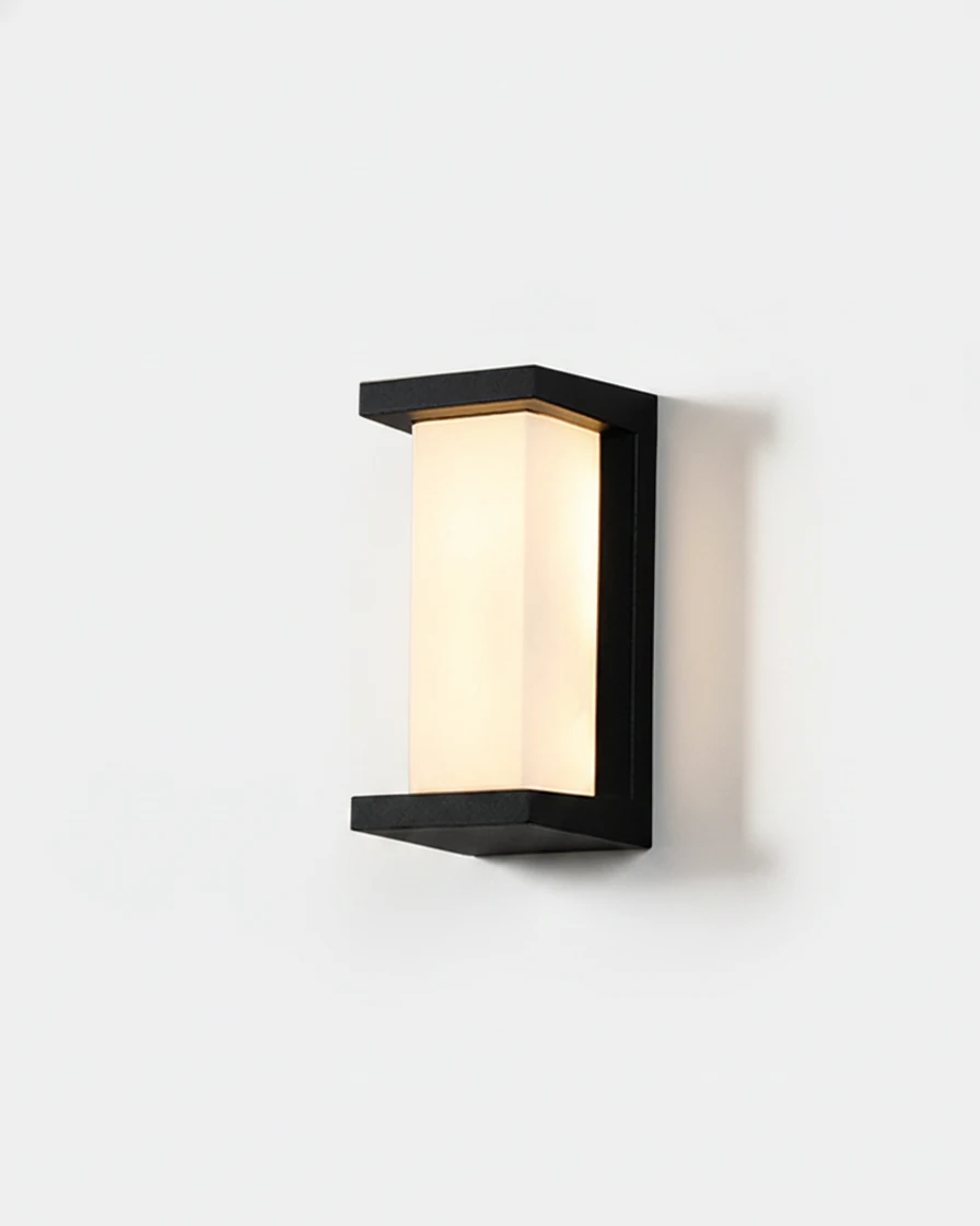 Outdoor wall sconce PORTICO No.02 Compact, black frame holding a lit opal column, mounted on a plain wall