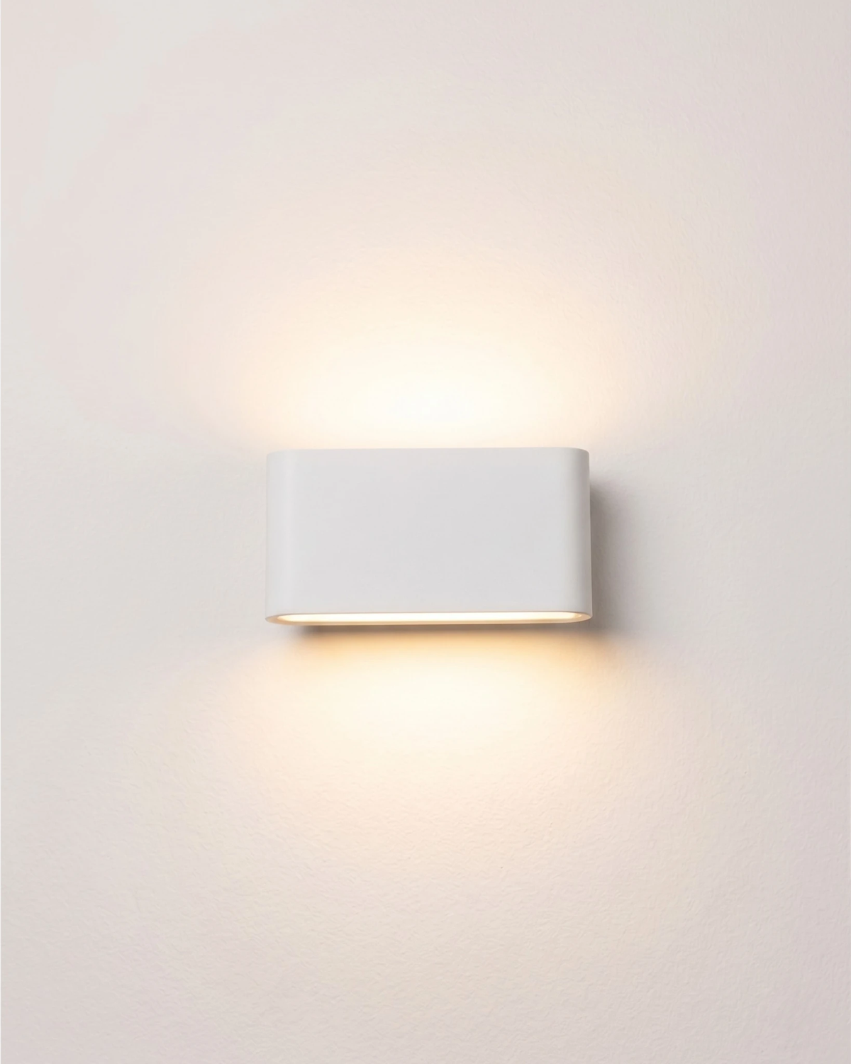 Outdoor wall sconce PISA No.01 medium size in matte white, lit pill-shaped body on a pale wall