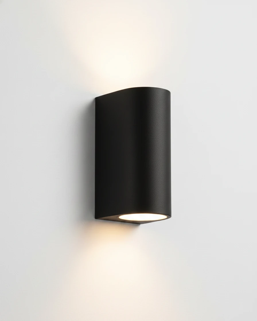 Outdoor wall sconce NOTO No.01, black half-cylinder body switched on with light washing up and down a white wall
