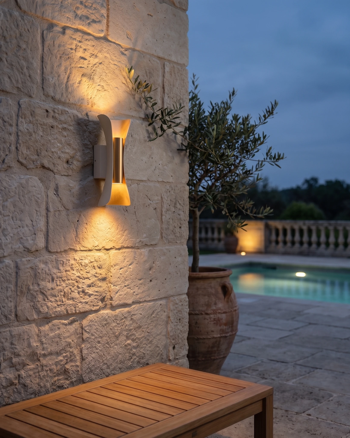 Outdoor wall sconce VENTO No.01 lit on a stone wall at dusk beside a wooden bench and a swimming pool