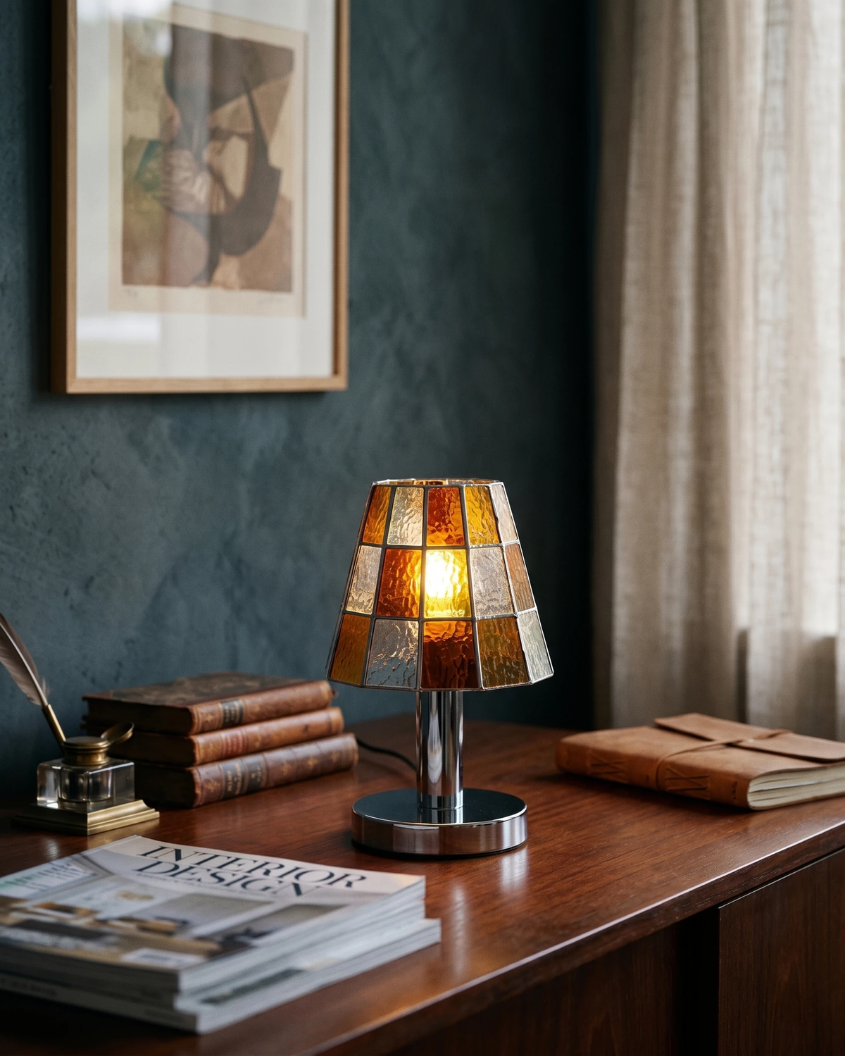 Stained glass table lamp VETRA No.01 in vibrant orange, lit on a walnut desk with old books and a dark green wall